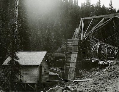 A wooden building and conveyor chute with forest in the background