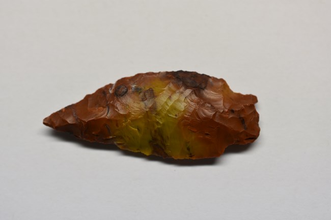 Brown projectile point showing markings from where it was carved out of stone.