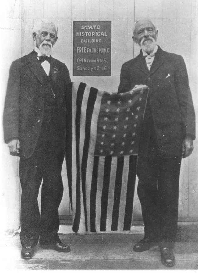 Two older men holding a United States flag between them.