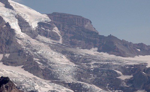 A large, flat-topped rock feature on a ridge above a glacier.