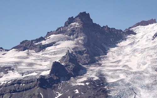 A sharp, triangular peak of crumbly dark rock along a ridge above a glacier.