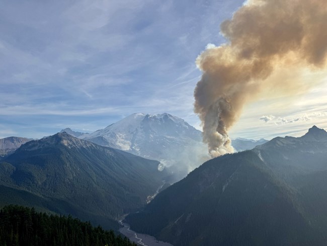 View of the White River Valley with billowing smoke from multiple fires, looking east toward Mount Rainier in the background.