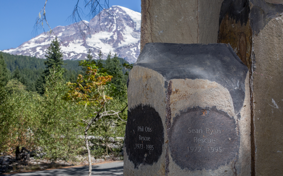 Two names inscribed into the top of a rough-hewn basalt column in front of a view of Mount Rainier.