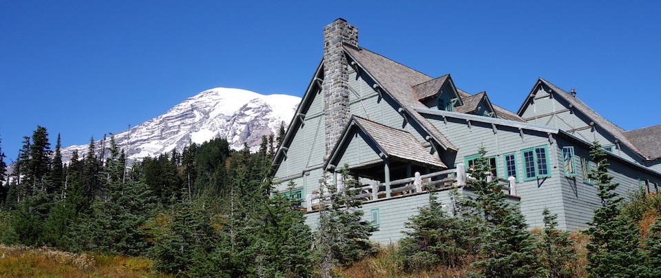 A large wood building with pitched roofs and a deck in front of Mount Rainier.