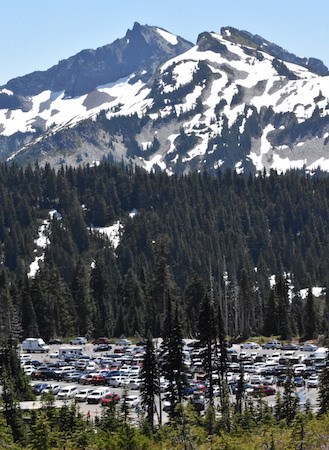 A full parking lot beneath forested slopes and rocky peaks.