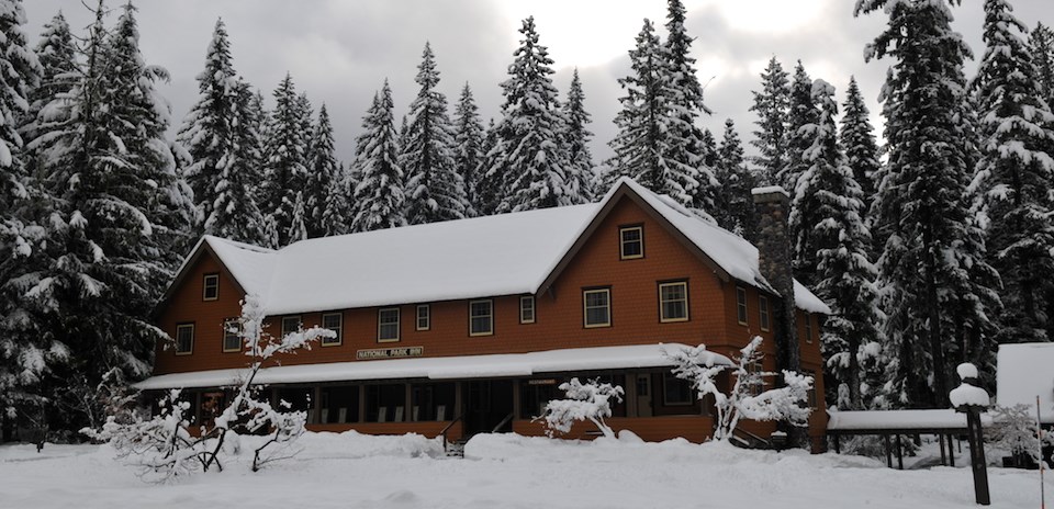 A wood building with pitched roofs covered in snow in a snowy forest.