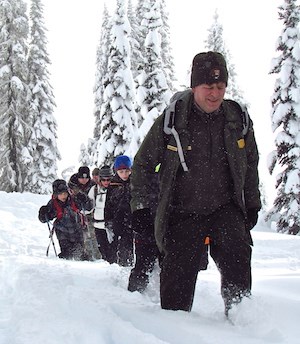 A ranger leads a group of people through  deep snow.