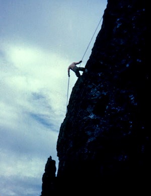 A climber braces against a rope as he ascends a steep cliff.