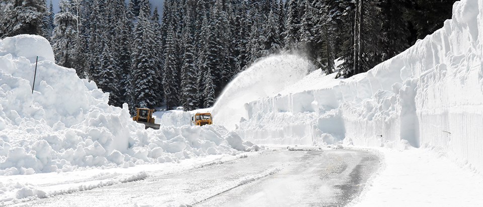 Two plows remove snow on partially snow covered road.