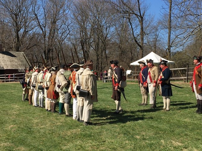 12 revolutionary war re-enactors soldiers standing in a line facing their commanders waiting for inspection by the five commanders.