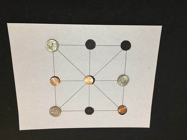 9 Men's Morris game being played with 3 quarters and 3 pennies as playing pieces.