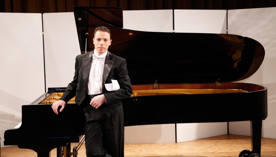 Photograph of Peter Toth in a black tuxedo and white tie standing by a grand piano