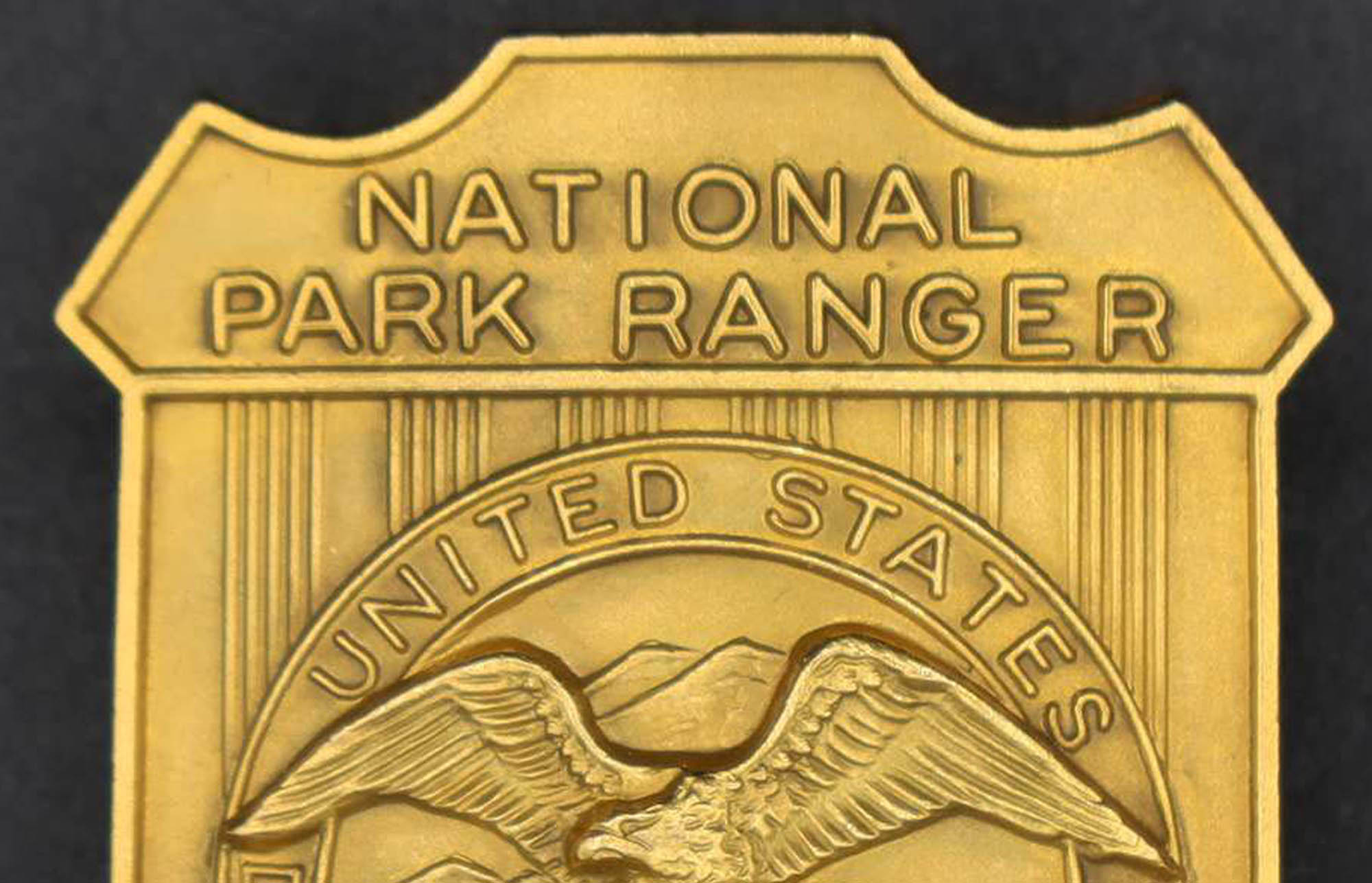 Gold shield-shaped badge marked National Park Ranger. The round seal in the middle has an eagle looking to its right.e