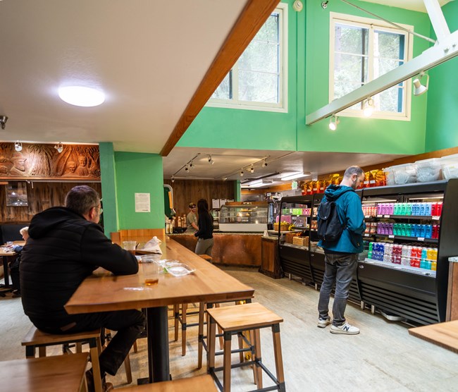 People eat and peruse food options in coolers at a cafe.