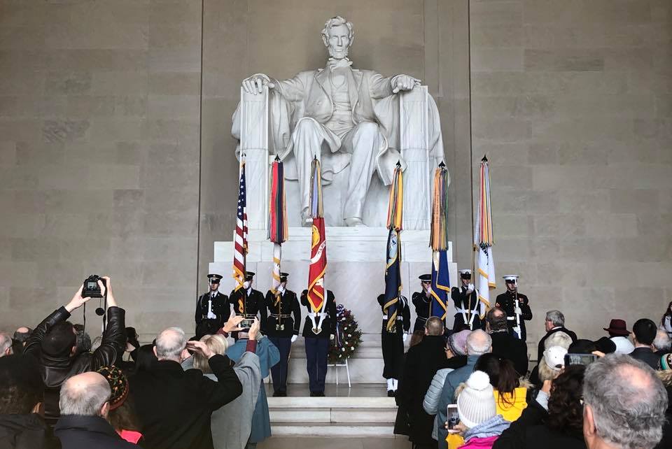 Members of the military in uniform holding flags in front of a large statue of Abraham Lincoln