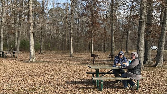 Picnic area with two people bundled up sitting at a picnic table.