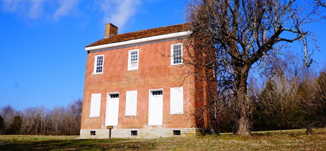 A orange brick two-story historic house and barren tree