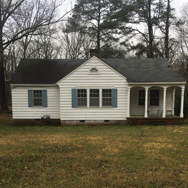 A one story white clapboard house with a covered porch and gray shutters.