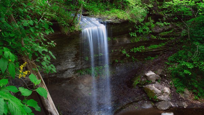 A thin waterfall flowing over a sheer, short cliff.