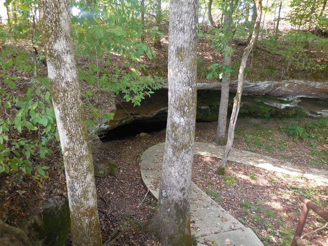 A winding paved path next to a large open cave.