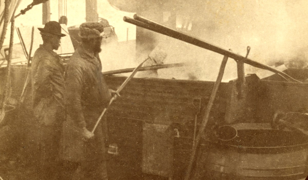 Two men fork blubber into the tryworks, a big oven-like structure on deck