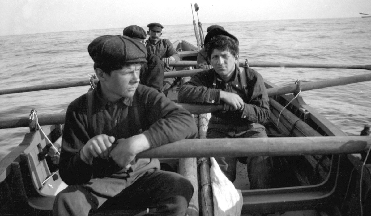 Black-and-white photo of men on whaleboat on open ocean.