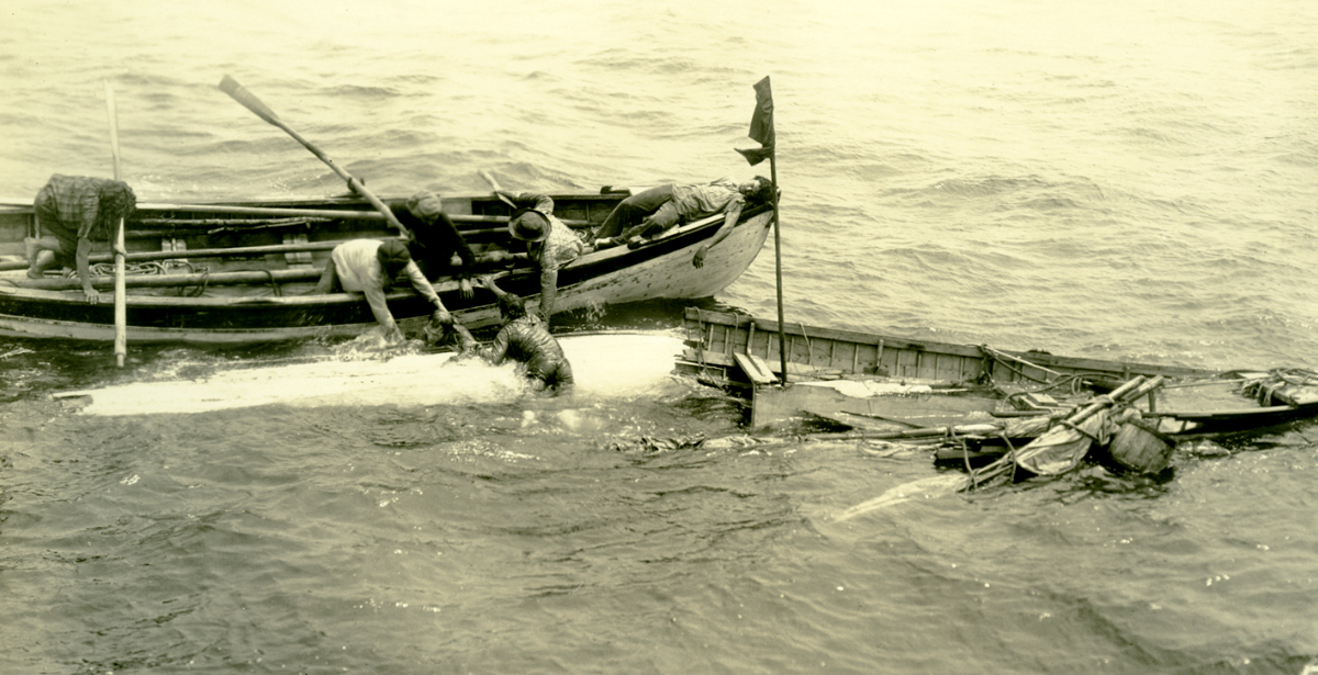 Men on whaleboat work to pull up a man who's been thrown overboard from his now smashed whaleboat.