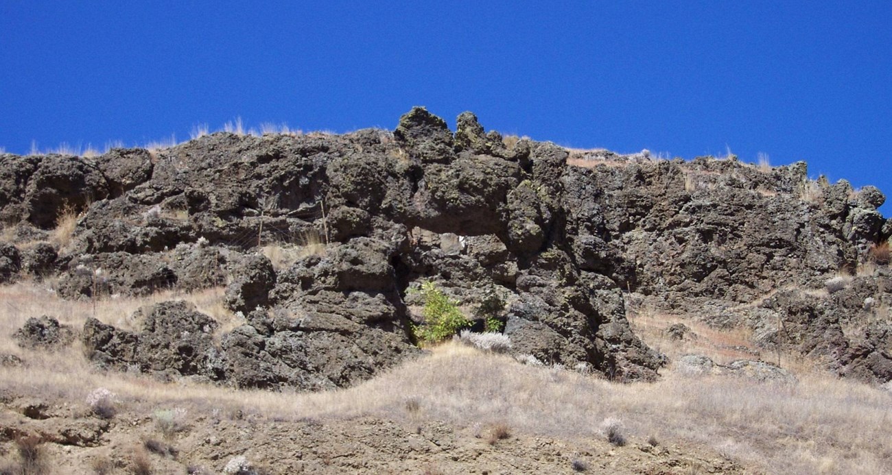 A basaltic rock outcropping on a hillside on a sunny day.
