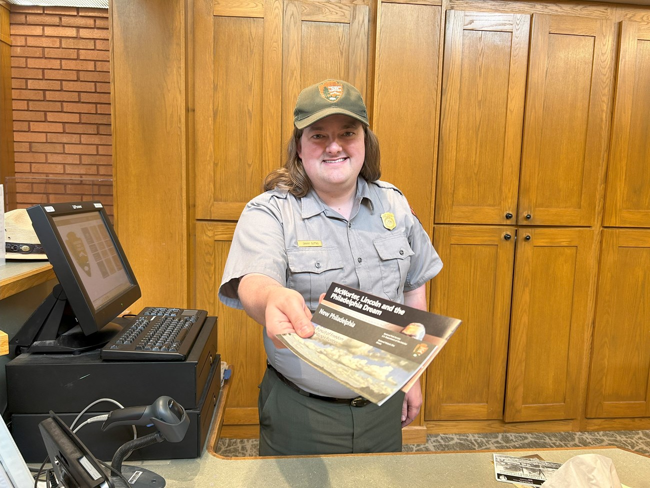 A park ranger leans over a counter and smiles at you as they hold out two brochures.