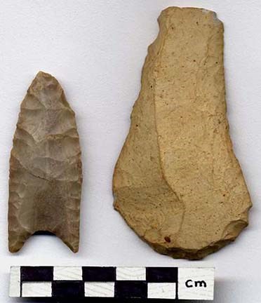 A narrow stone arrowhead and brown curved smooth piece of rock