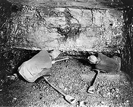 historic photo of two coal miners crouched down in a mine using picks