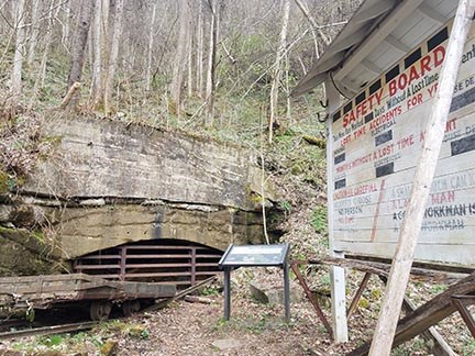a gated mine entrance with old mine car and safety board