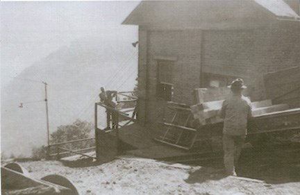historic photo of a man standing next to a building perched on a steep hillside