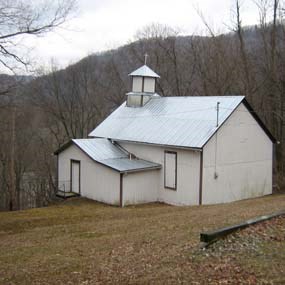 A white wooden church sitting on the side of a brown barren hill.