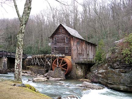 A wooden building with a water wheel next to a small creek.