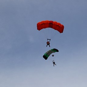 Two people with an orange parachute and a green parachute parachuting through the blue sky
