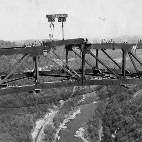 Workers connecting large metal beams of the bridge together far above a river below