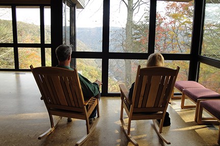 A man and a woman are sitting in two rocking chairs in front of a large window overlooking the gorge