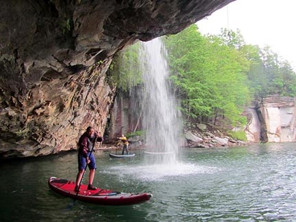 stand up paddle boarders paddle under a waterfall
