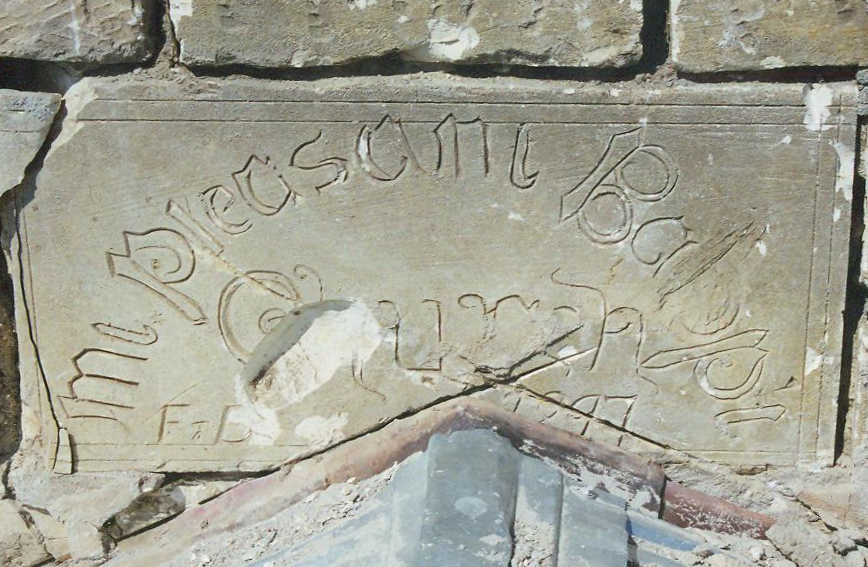 Photo of a large, chipped limestone brick above a church entrance. There is rough Gothic-style text engraved on the stone that reads: "Mt. Pleasant Babpt. Church F+D 1897".