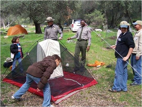 People working together to set up a tent on a green open area of grass.