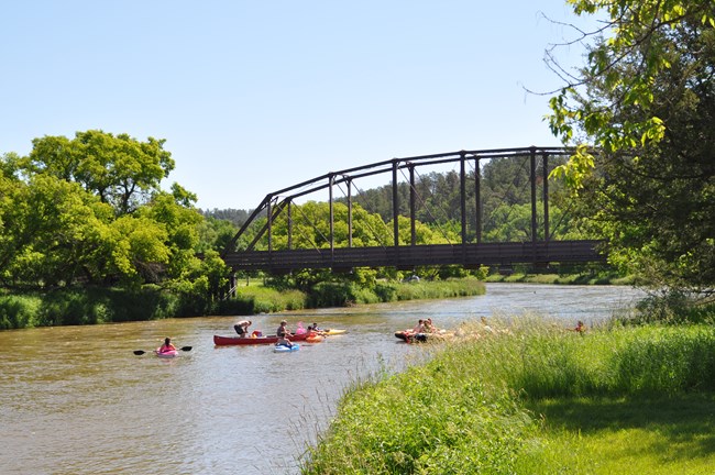 Canoes coming around a river bend, a bridge in the background.