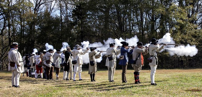 Living historians fire muskets towards the woods.