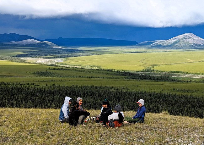 Teenagers with the Arctic Travelers program sit on a hillside looking into the southwest portion of Noatak National Preserve.