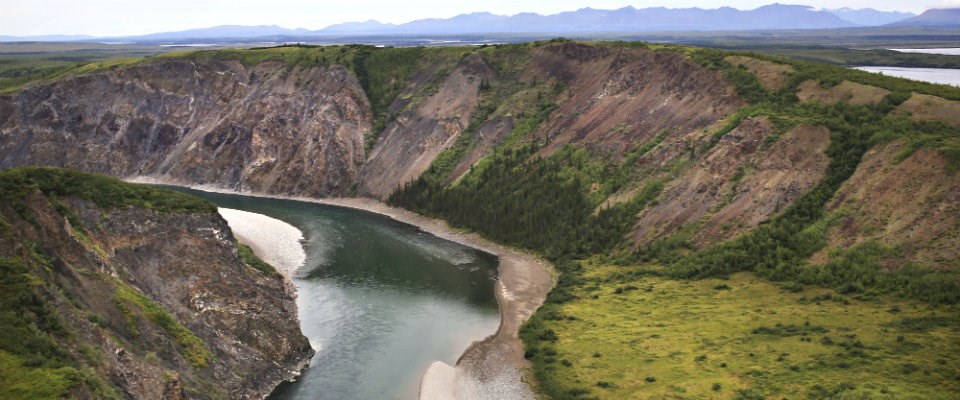 Noatak River flowing through the Grand Canyon of the Noatak on an overcast day. The surrounding tundra is green.