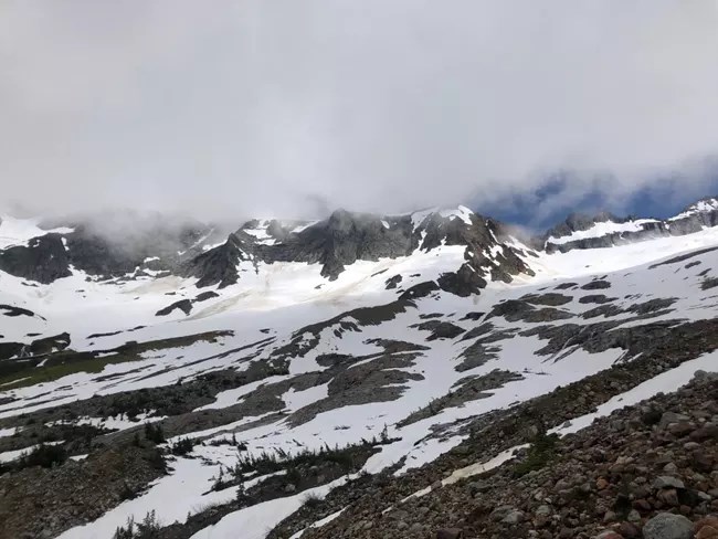 Cloud hovering over patchy snowfield and rocky slope