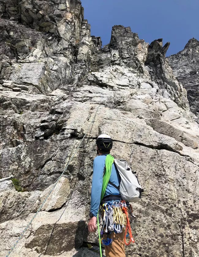 Ranger looking up a steep rock face with a rope hanging on it