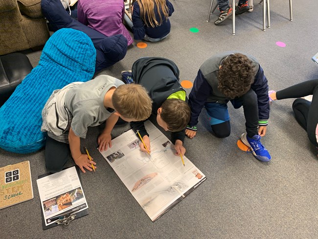 Four students sit on the floor looking at a map of a park