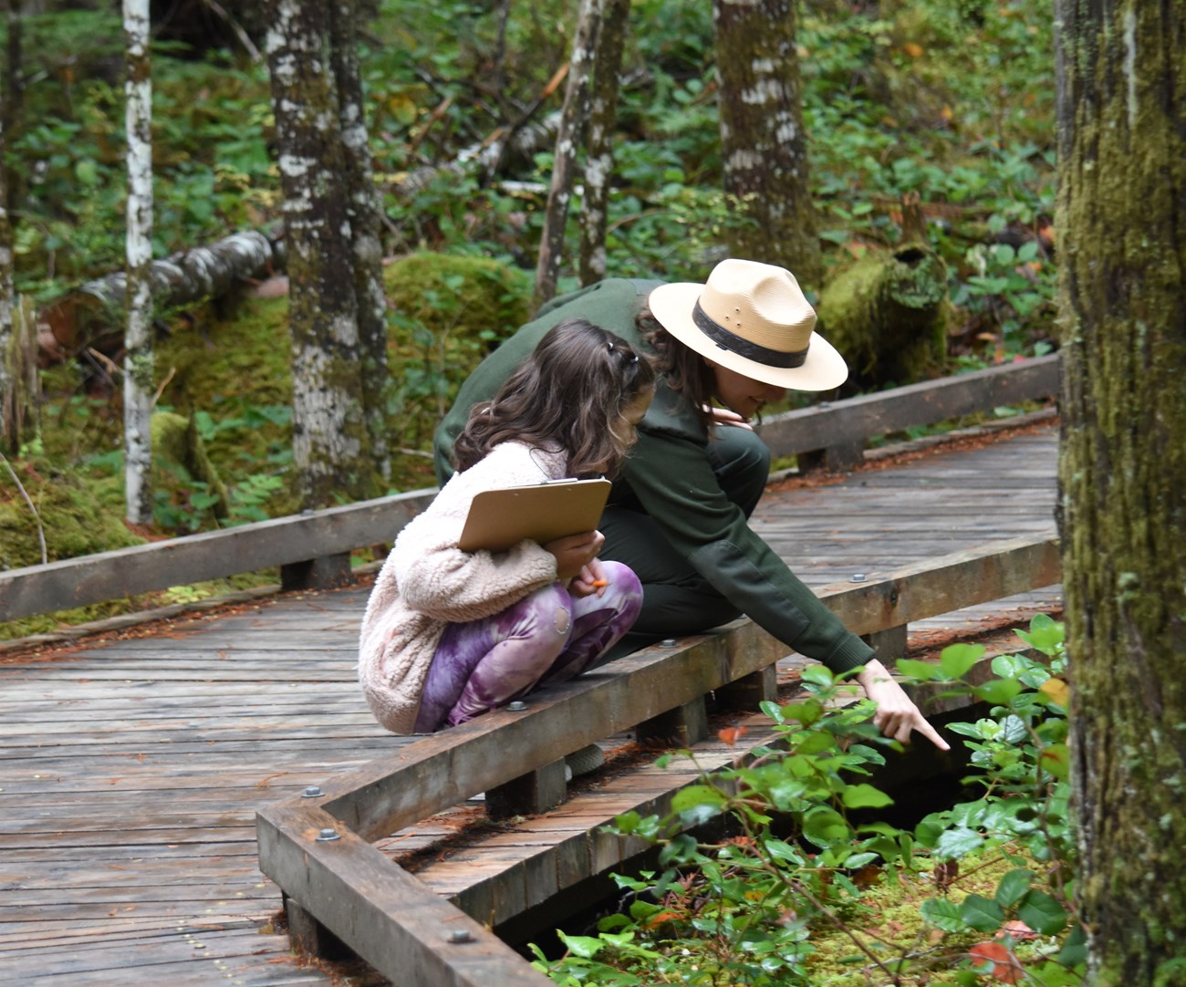 a ranger kneeling with a child while pointing at a fern