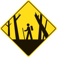 A yellow diamond warning sign with a hiker and hazardous trees.